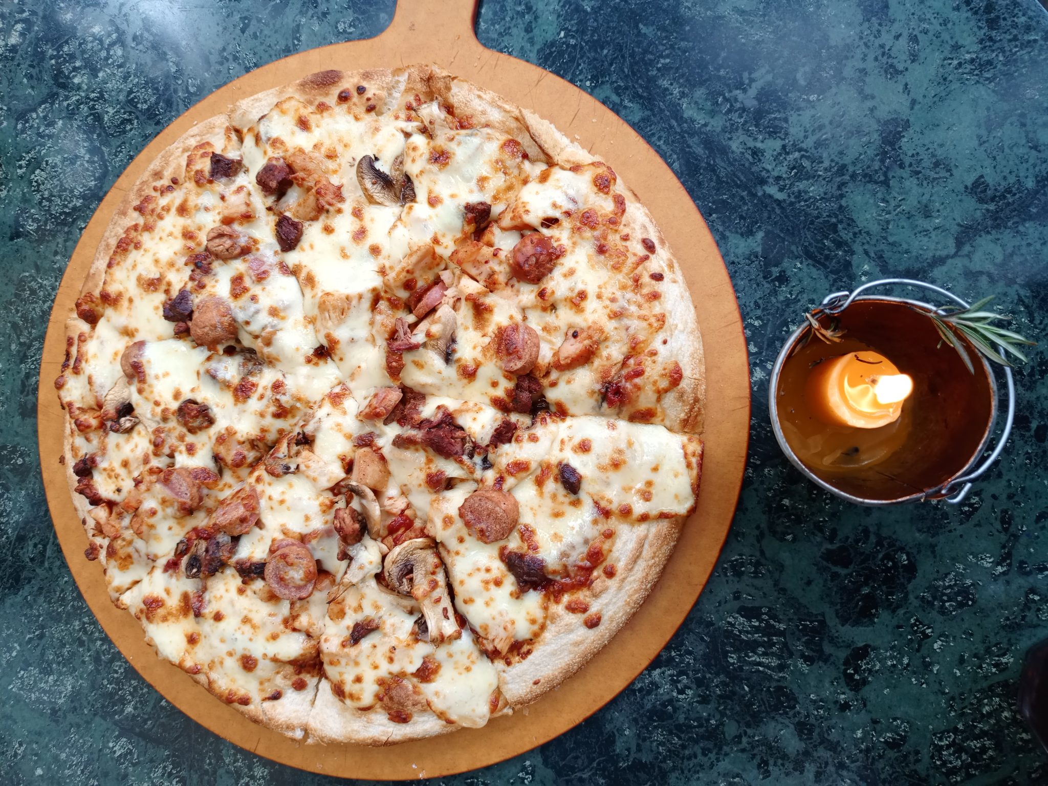 A whole pizza topped with melted cheese, sliced mushrooms, sausage pieces, and s